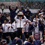 UConn Huskies center Donovan Clingan (32) hold up the championship trophy as the team celebrates in front of a large crowd of fans after the teams victory parade.