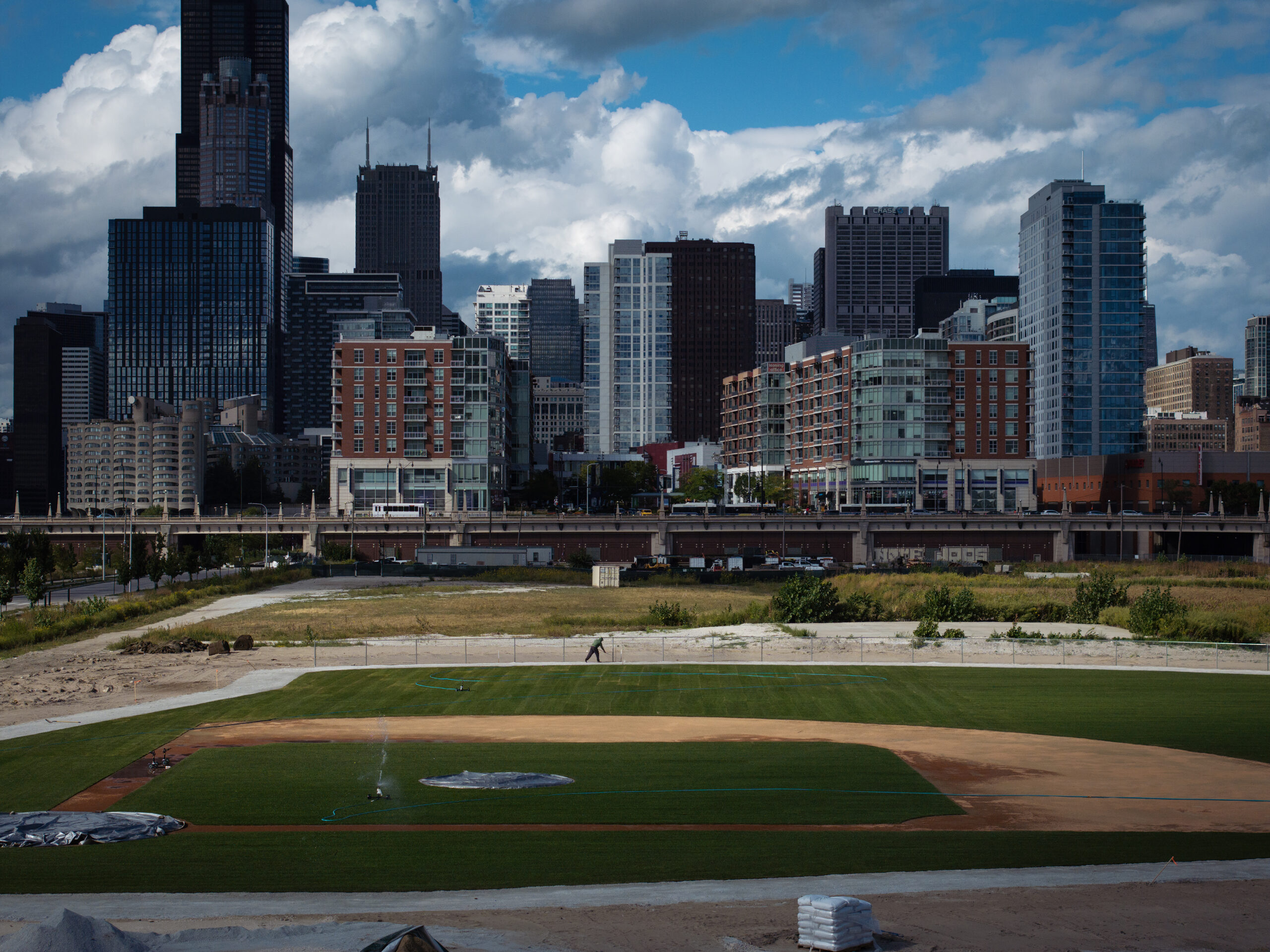 A groundskeeper tends to a baseball field that has arisen...