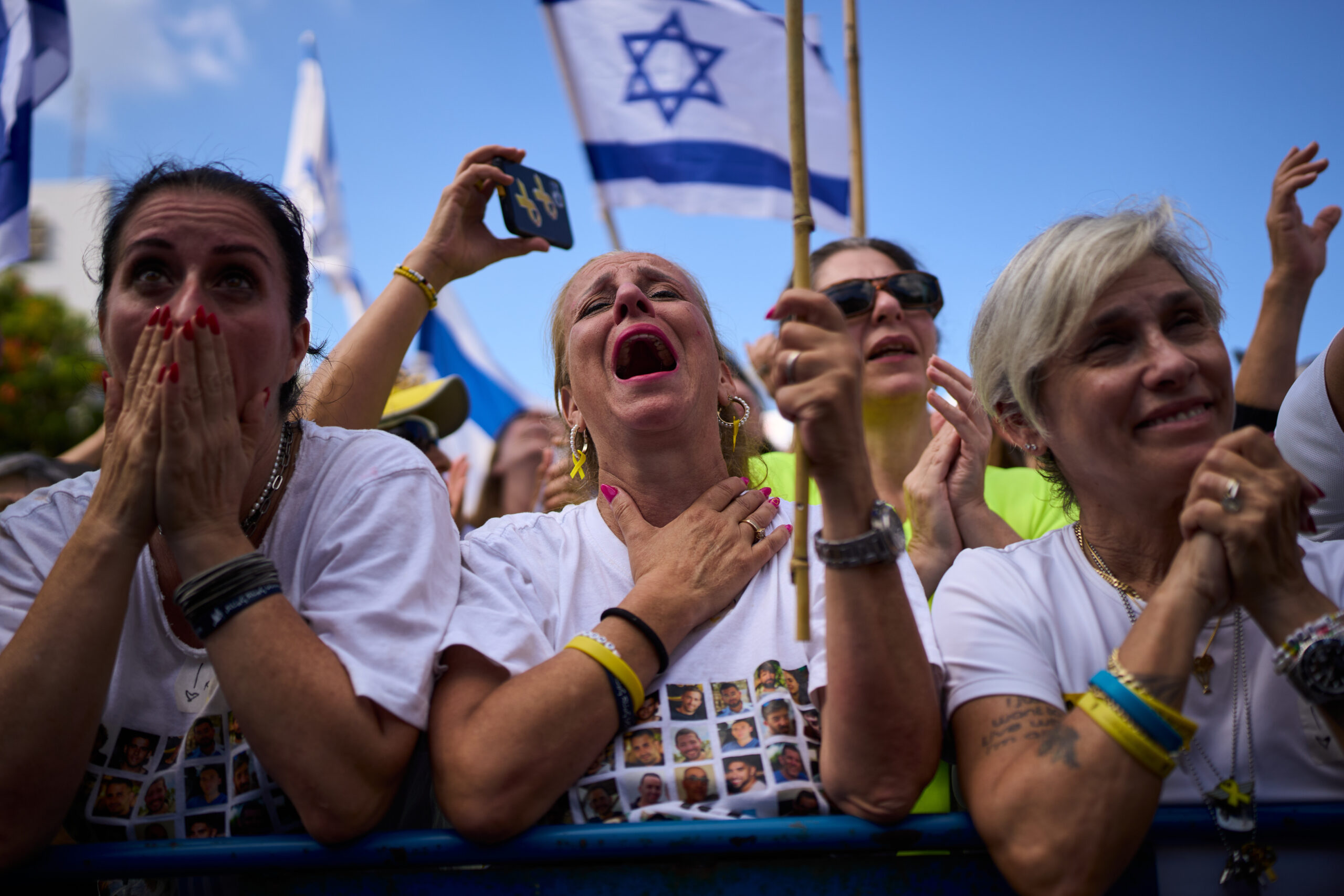 People react as they watch a live broadcast of Israeli...